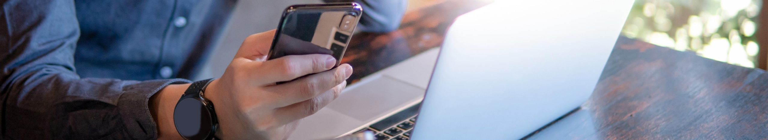 Male-hand-holding-smartphone.-Businessman-using-laptop-computer-and-digital-tablet_banner2-scaled